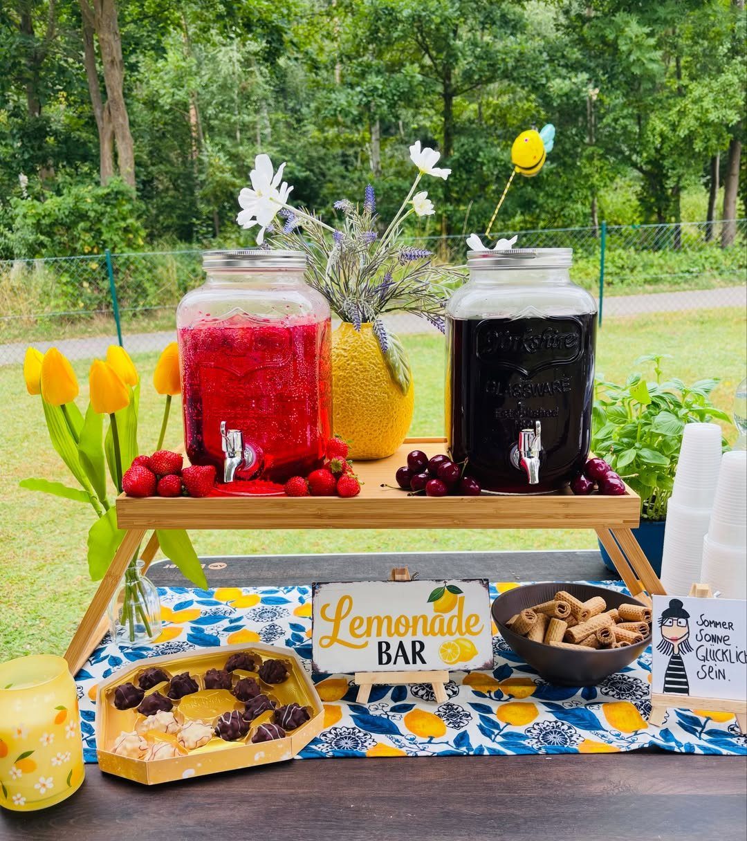 Lemonade bar with red and purple drinks, fresh berries, and lemon-patterned tablecloth.
