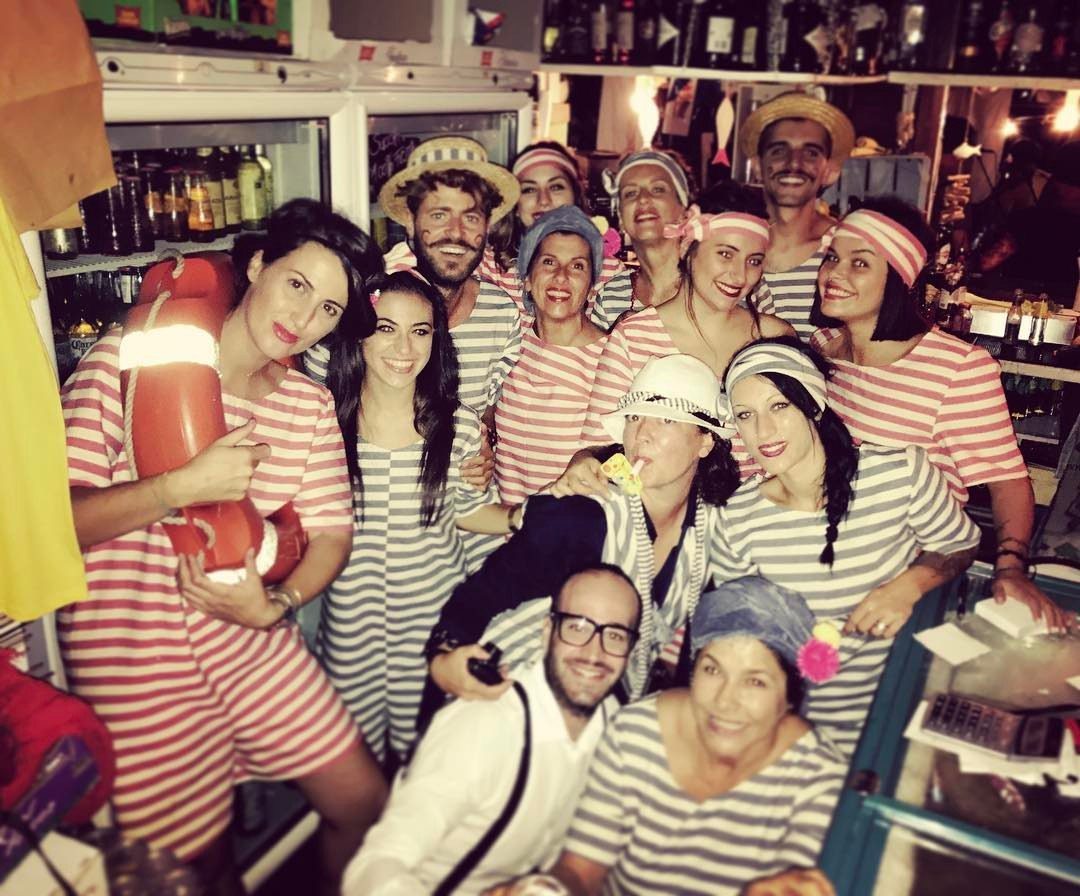 Group of people in striped nautical outfits posing with a lifebuoy indoors.