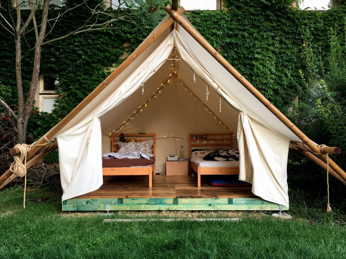 Canvas bell tent with wooden beds and fairy lights set on a green lawn