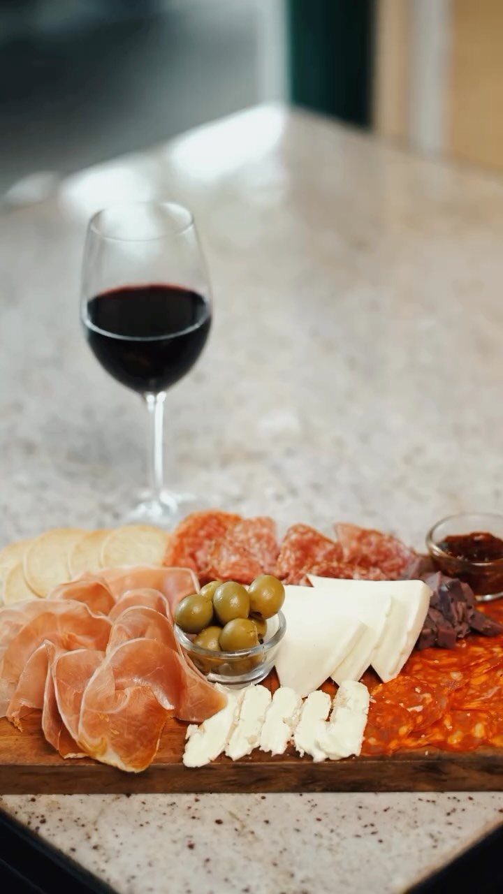 Charcuterie board with meats, cheeses, and olives next to a glass of red wine.