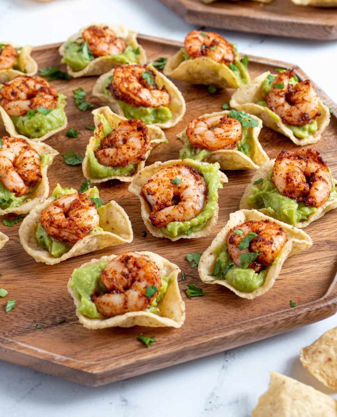 Grilled shrimp with guacamole on tortilla chips served on a wooden board