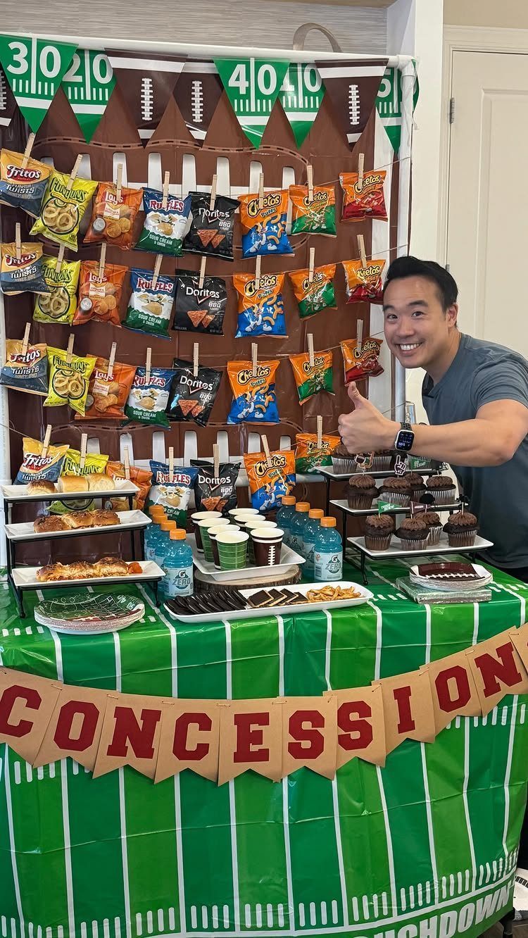Football-themed concession stand with hanging chips, appetizers, and a green field tablecloth.