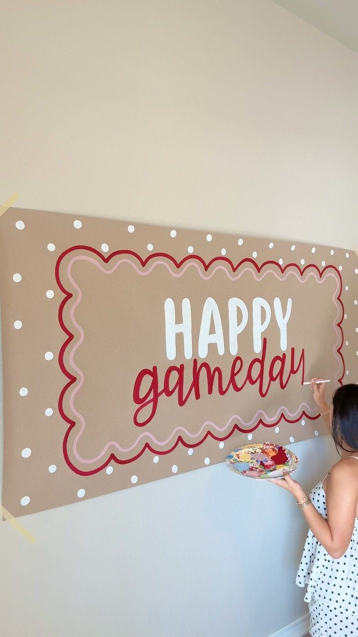 Woman painting a brown Happy Gameday banner with red borders on a wall