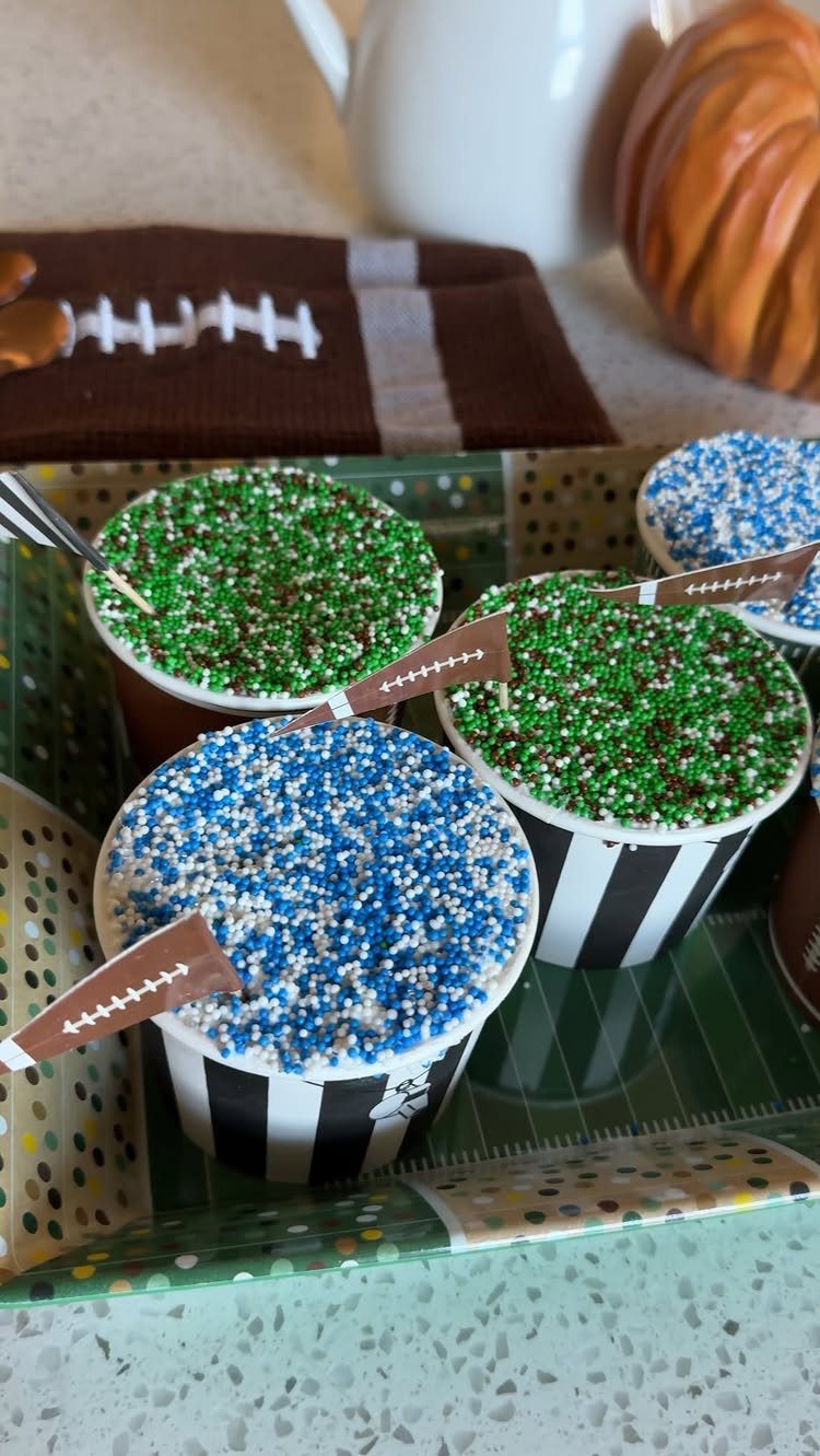 Cupcakes with blue and green sprinkles and football toppers in striped cups.