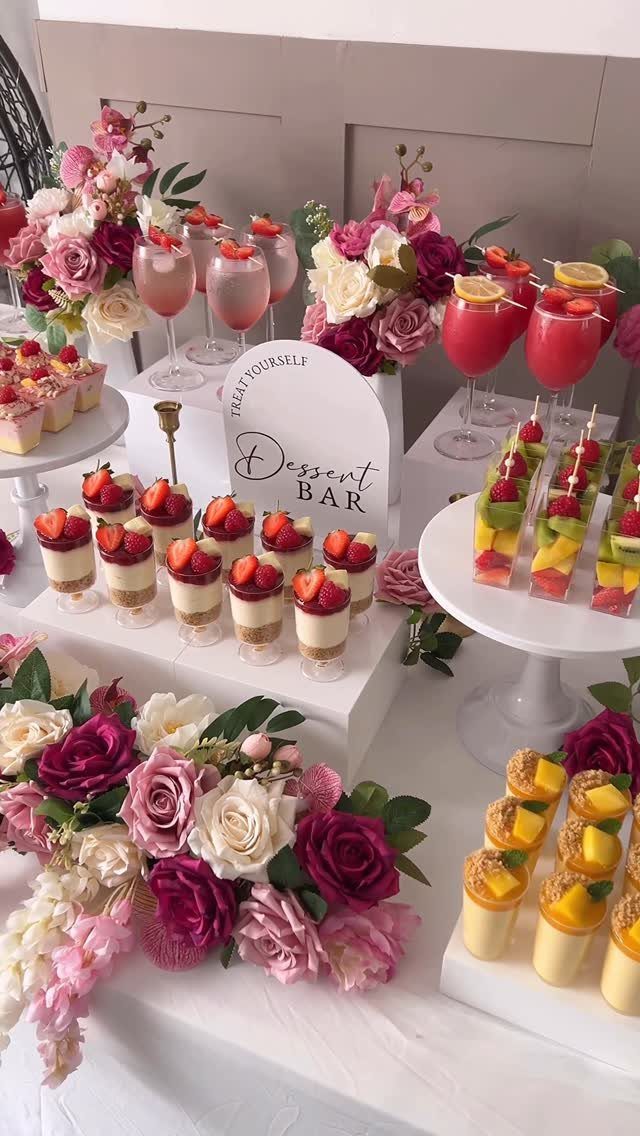 Dessert bar table with strawberry parfaits, fruit skewers, cocktails, and pink roses.