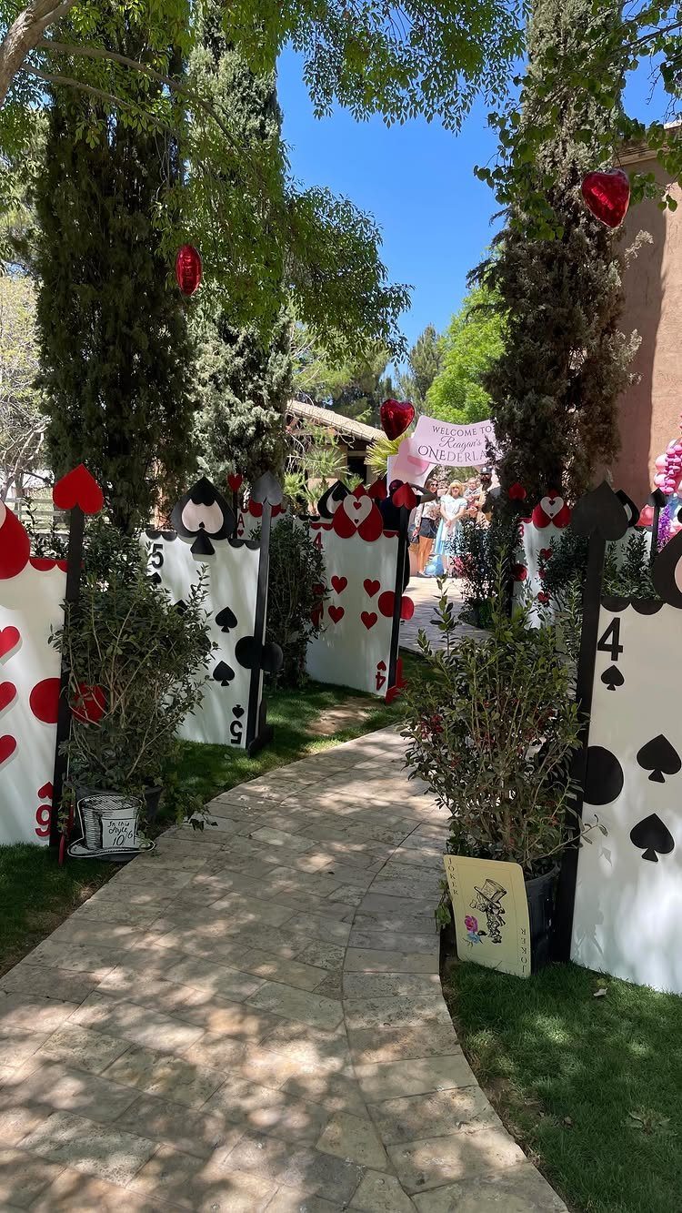 Stone garden path decorated with oversized playing cards and greenery under a blue sky.
