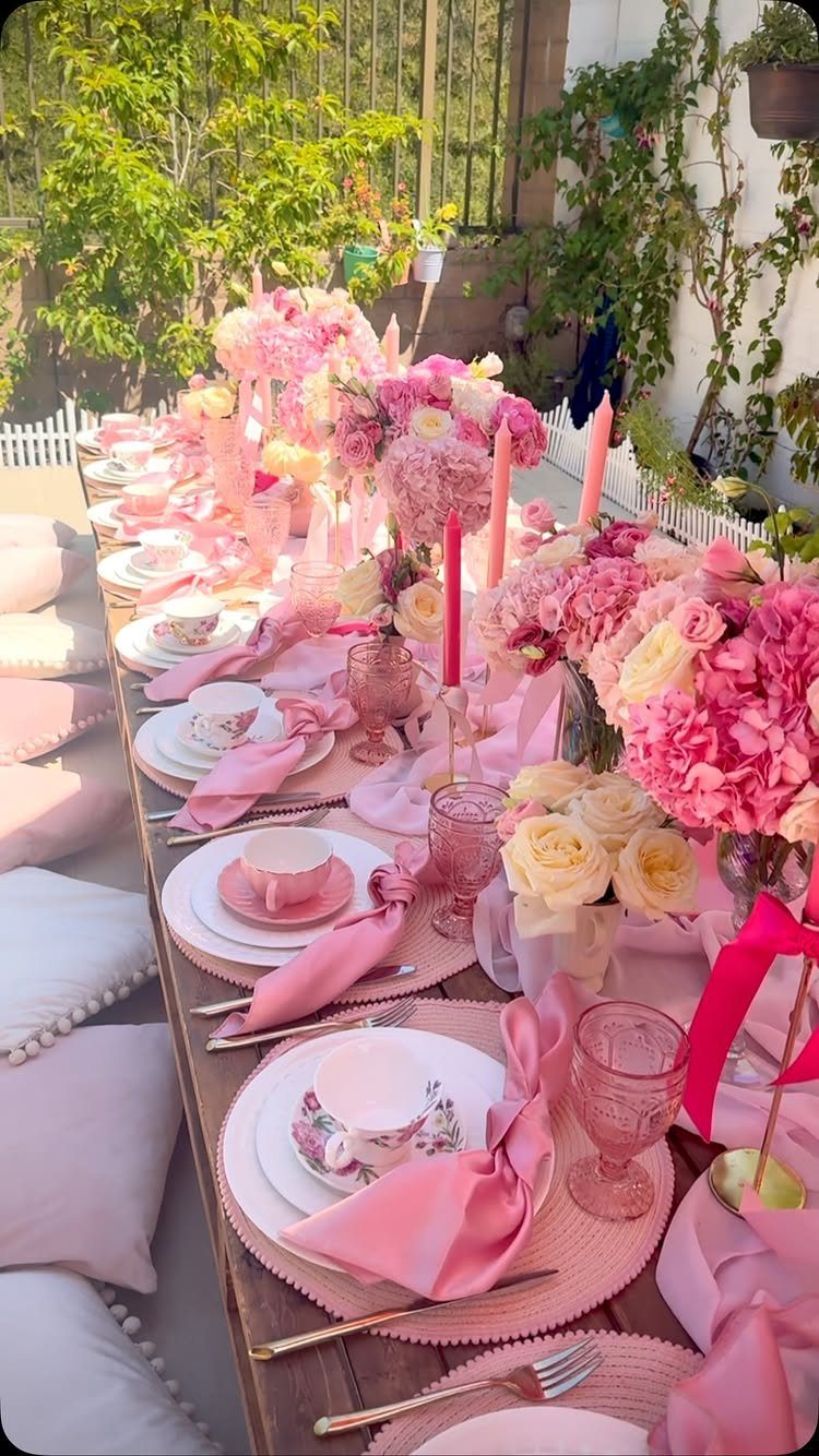 Pink tea party table setting with flowers and cushions in a sunny garden