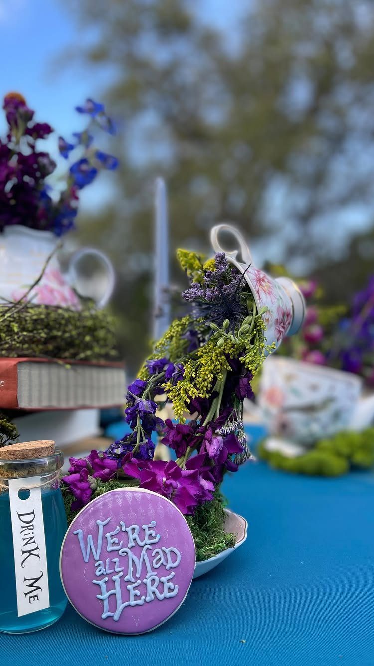 Whimsical tea party table with tipped teapots, purple flowers, and Alice in Wonderland treats.