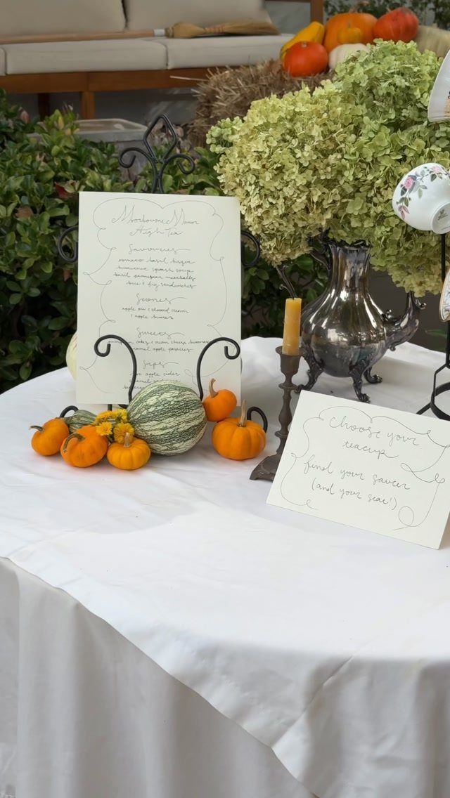 Autumn tea party table setting with pumpkins, silver teapot, and floral teacup outdoors.