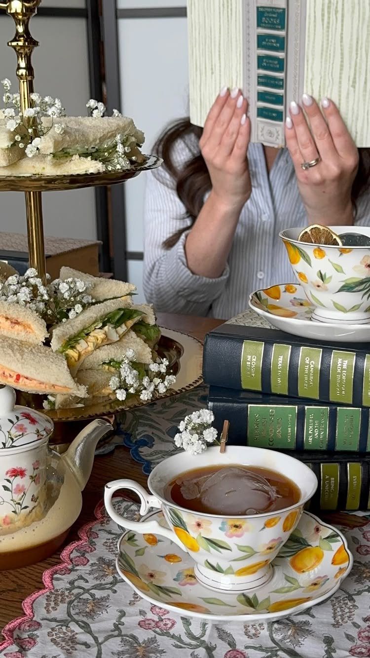 Woman reading a book behind a tea service with sandwiches and hardcover books.