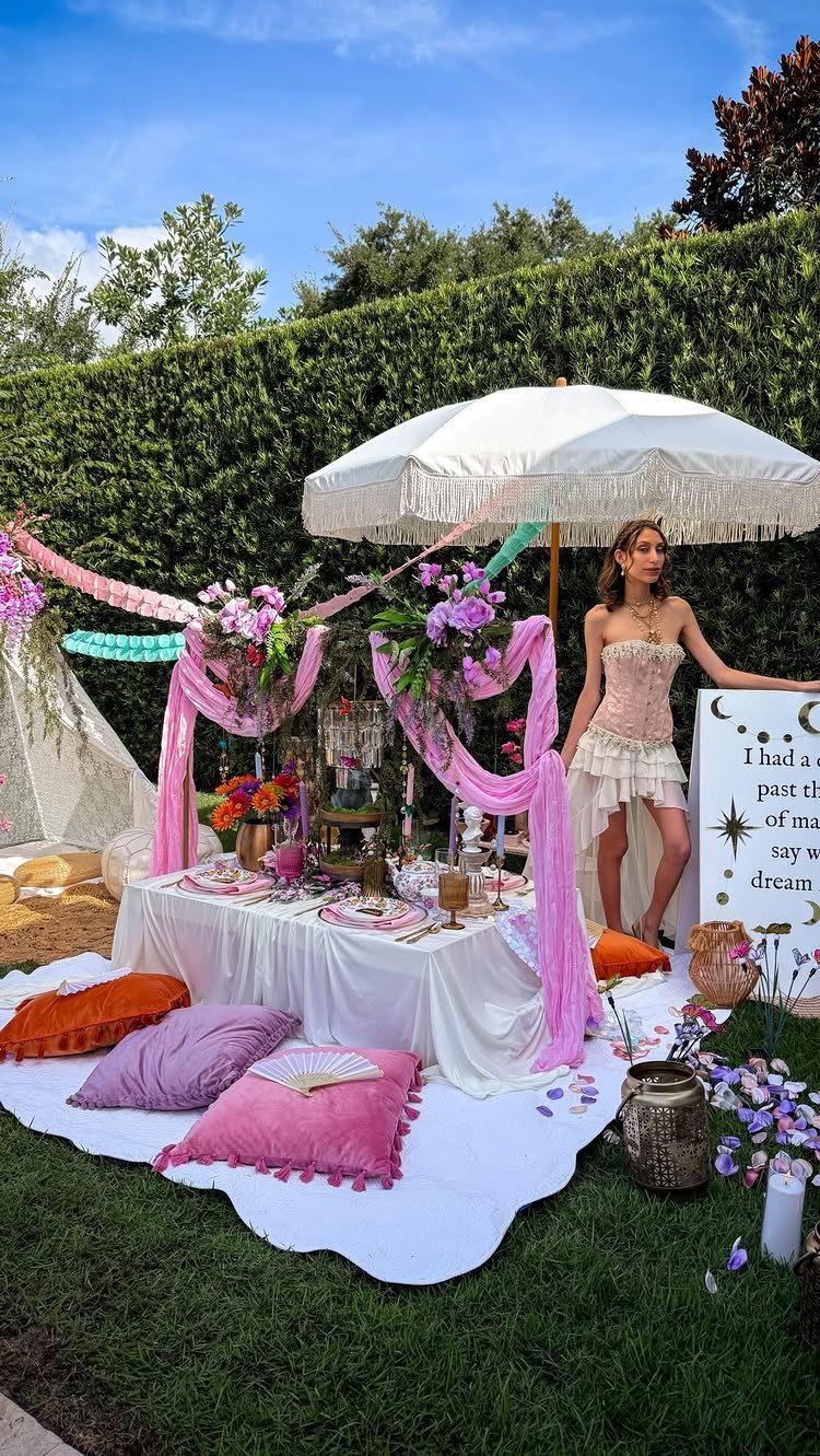 Whimsical outdoor tea party setup with pink fabrics, flowers, and a woman posing.