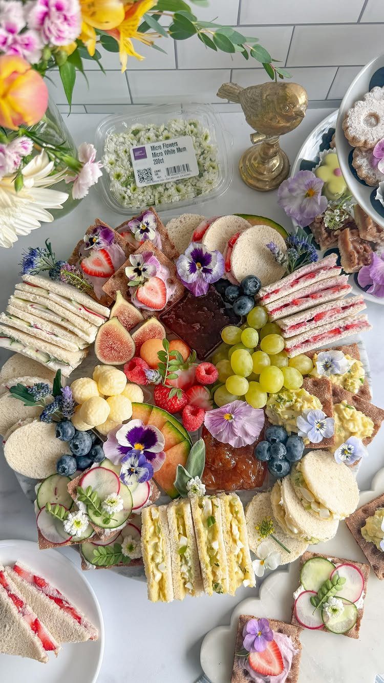 Platter of finger sandwiches, fresh fruits, and pastries decorated with edible flowers.
