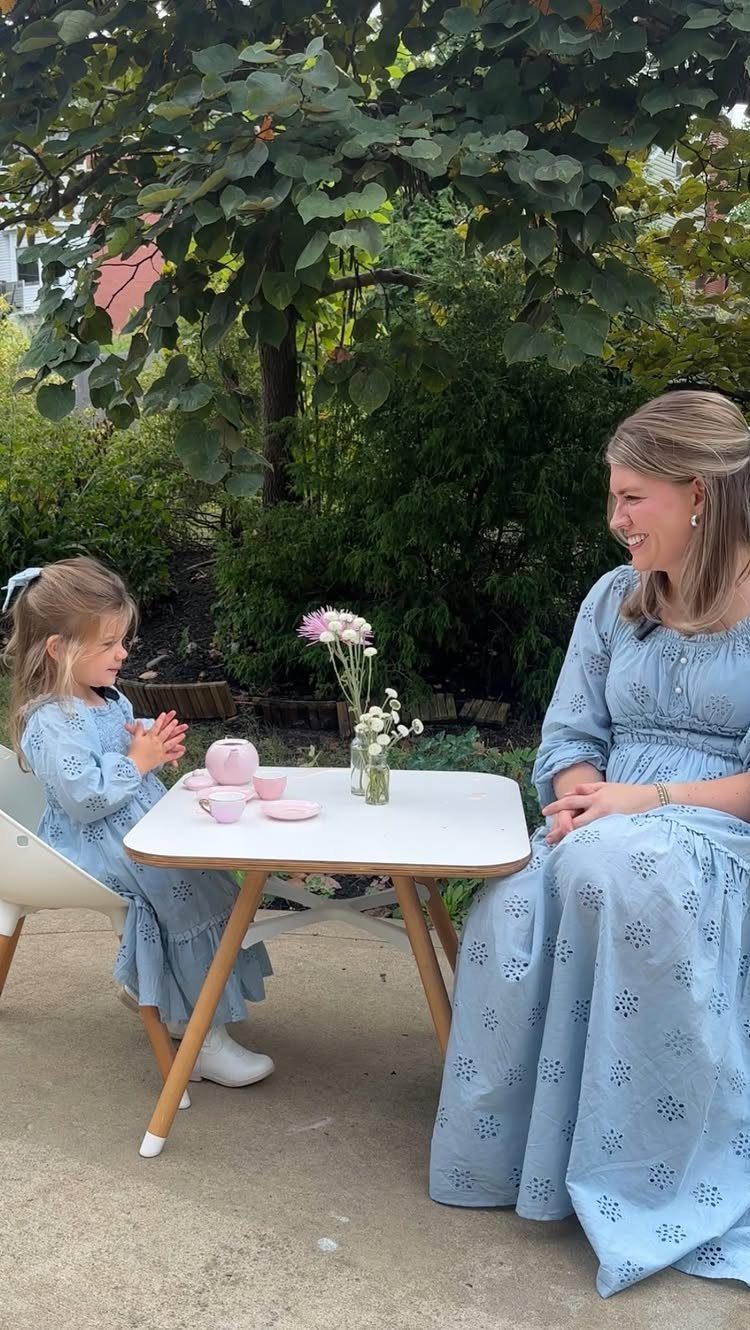 Woman and young girl in matching blue dresses having tea at a small table.