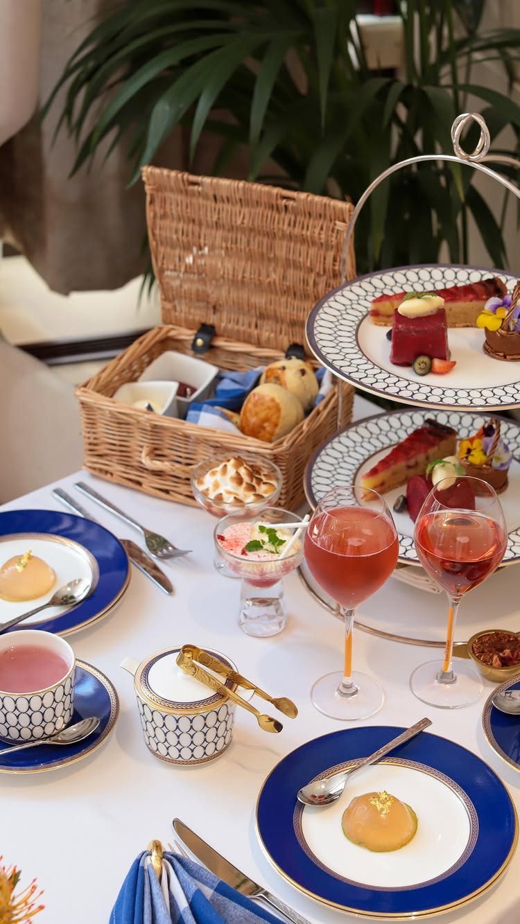 Elegant tea service with blue-rimmed plates, desserts on a stand, and a wicker basket.