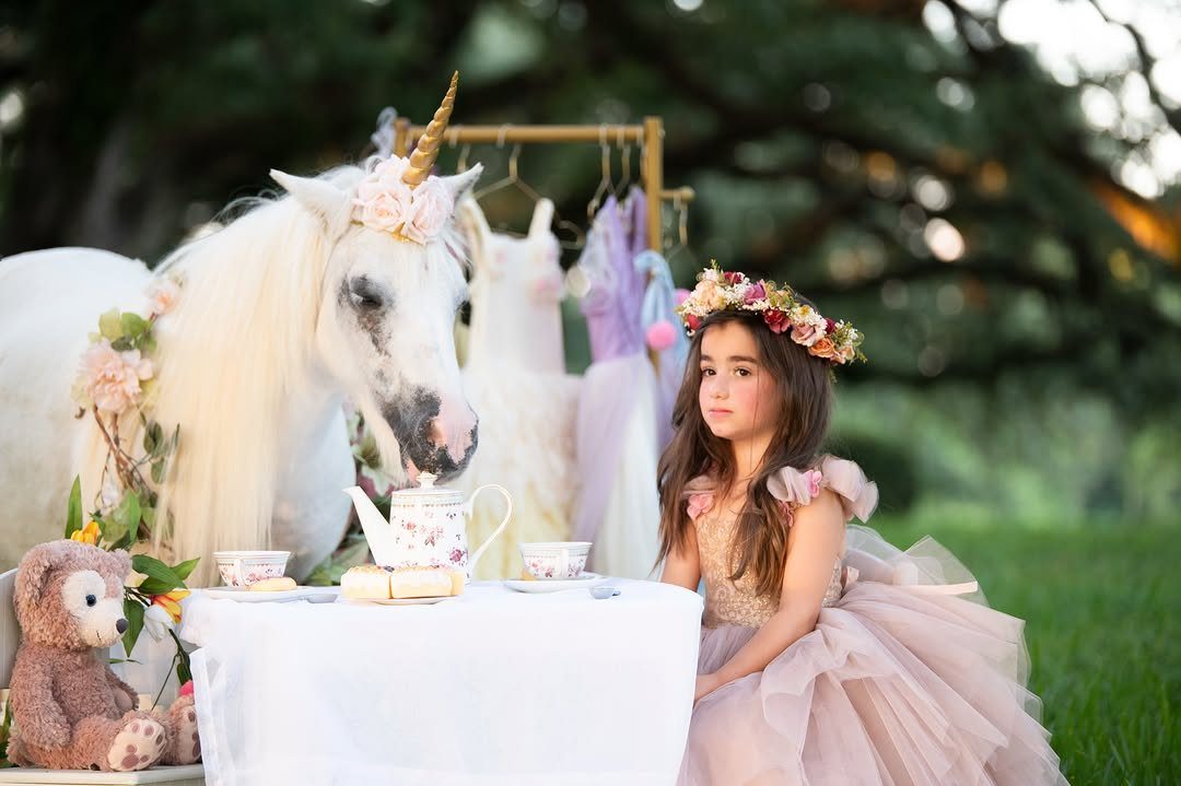 Girl in pink dress and white unicorn horse at an outdoor tea party