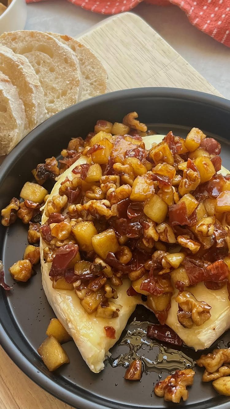 Melted brie cheese topped with apples, cranberries, and walnuts on a black plate.