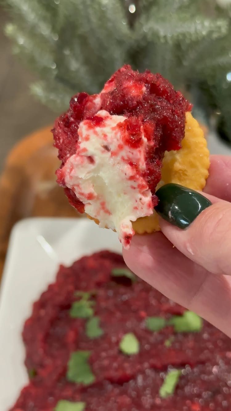 Cracker topped with white cream cheese and red cranberry dip held by hand.