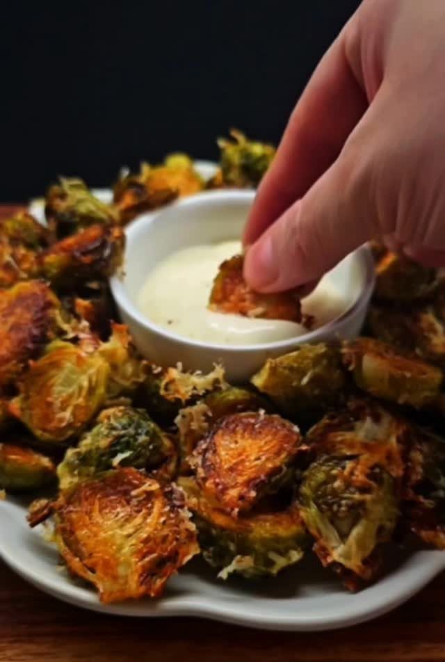 Roasted brussels sprouts on a white plate with a creamy dipping sauce bowl.