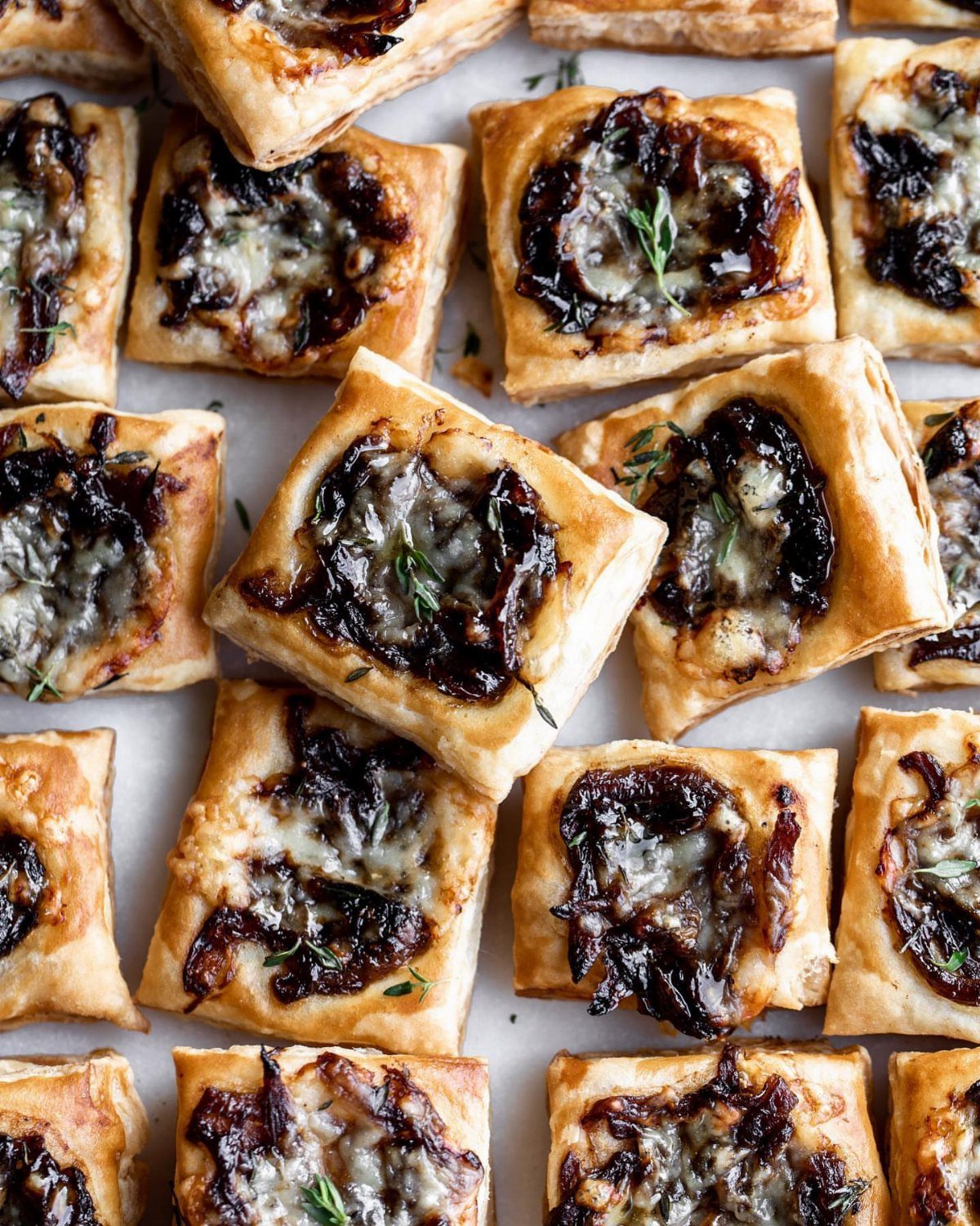 Caramelized onion and cheese puff pastry tartlets garnished with fresh thyme leaves.