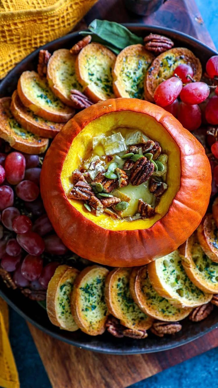Pumpkin filled with creamy dip and seeds surrounded by toasted bread and grapes