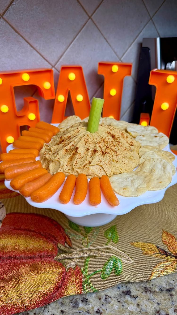 Orange pumpkin hummus on a white platter with baby carrots and pita chips.