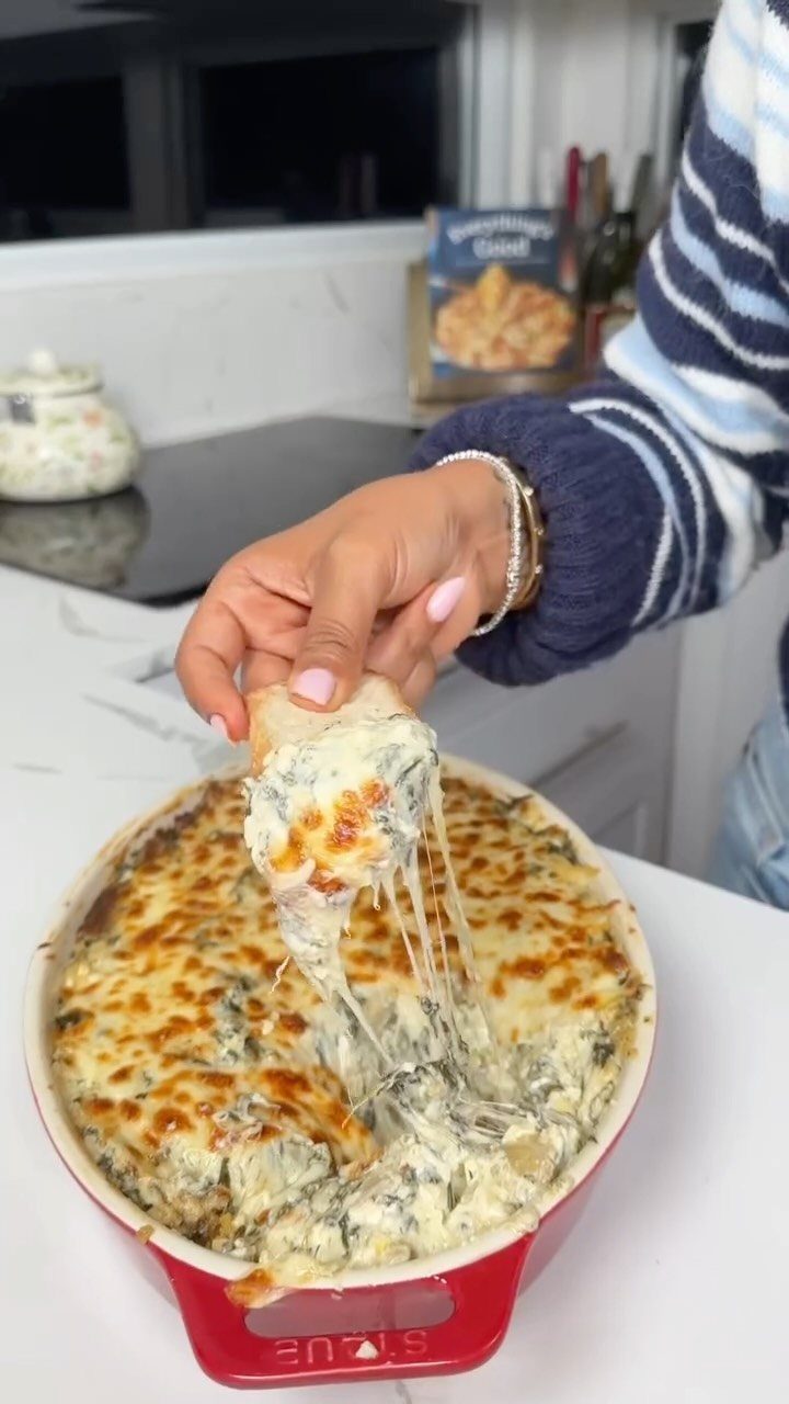 Creamy spinach artichoke dip in a red dish with a cheesy bread scoop.