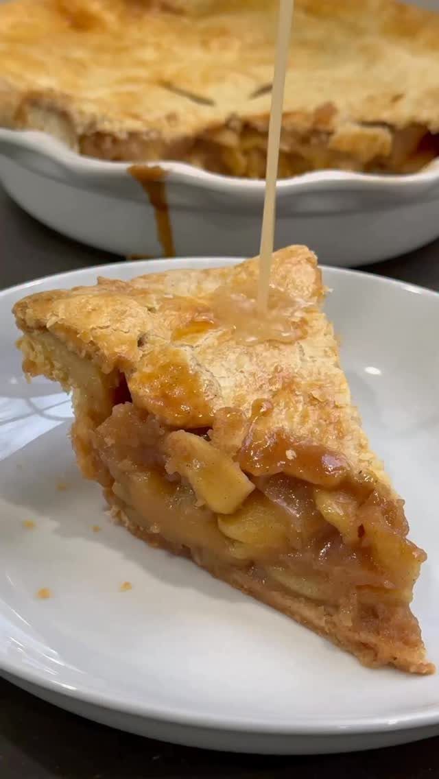 Slice of apple pie on a white plate with caramel sauce being poured.