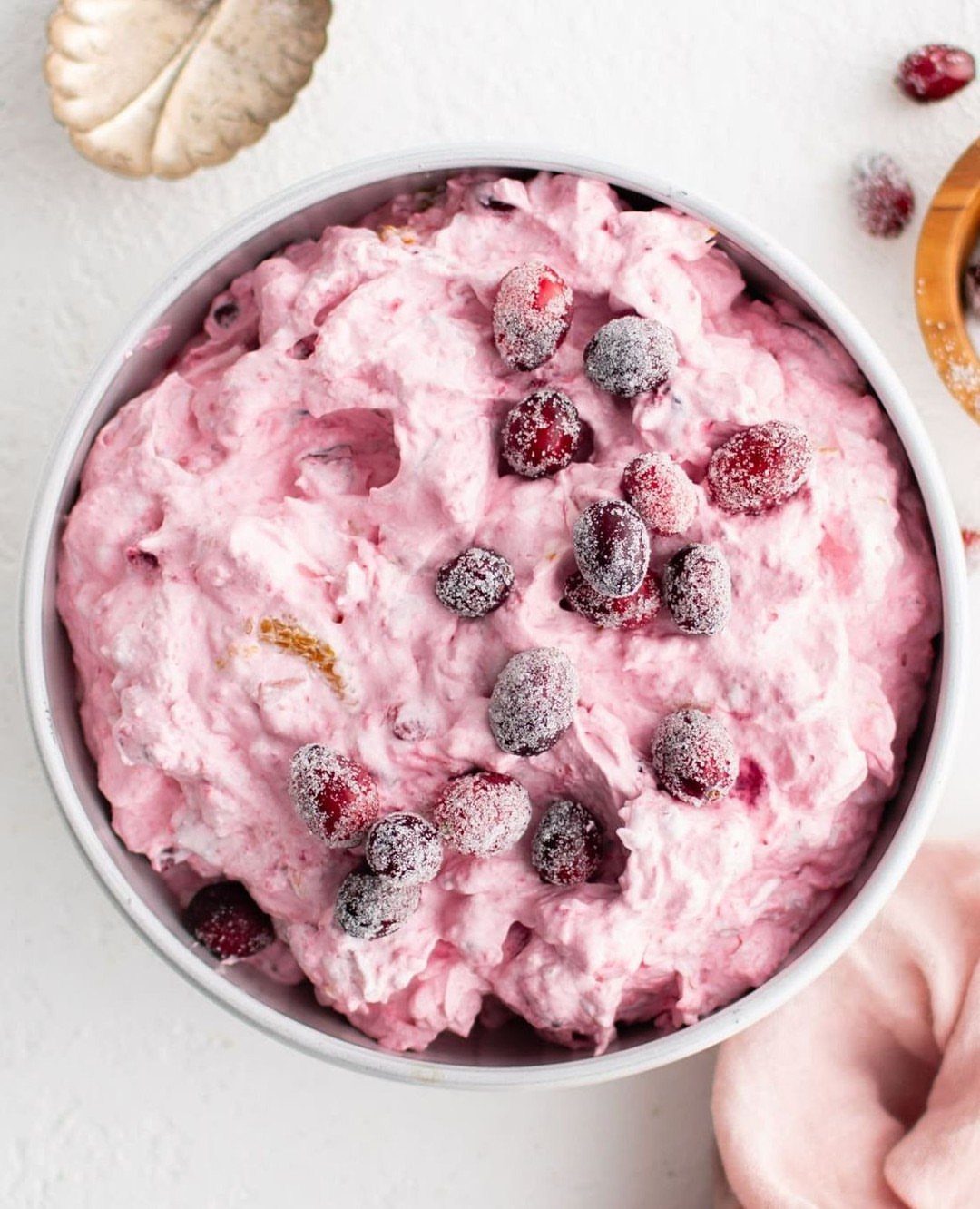 Pink cranberry fluff salad in a white bowl topped with frosted cranberries