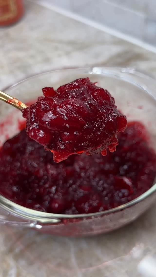 Deep red chunky cranberry sauce being lifted by a gold spoon from a bowl.