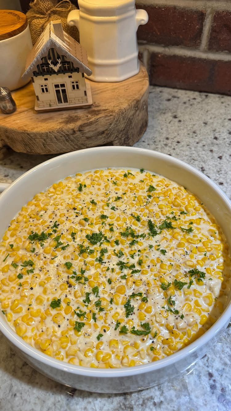 Creamed corn in a white bowl topped with fresh parsley on a countertop.