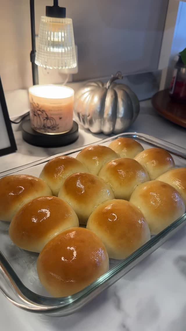 Golden-brown dinner rolls in a glass baking dish with a silver pumpkin decoration.