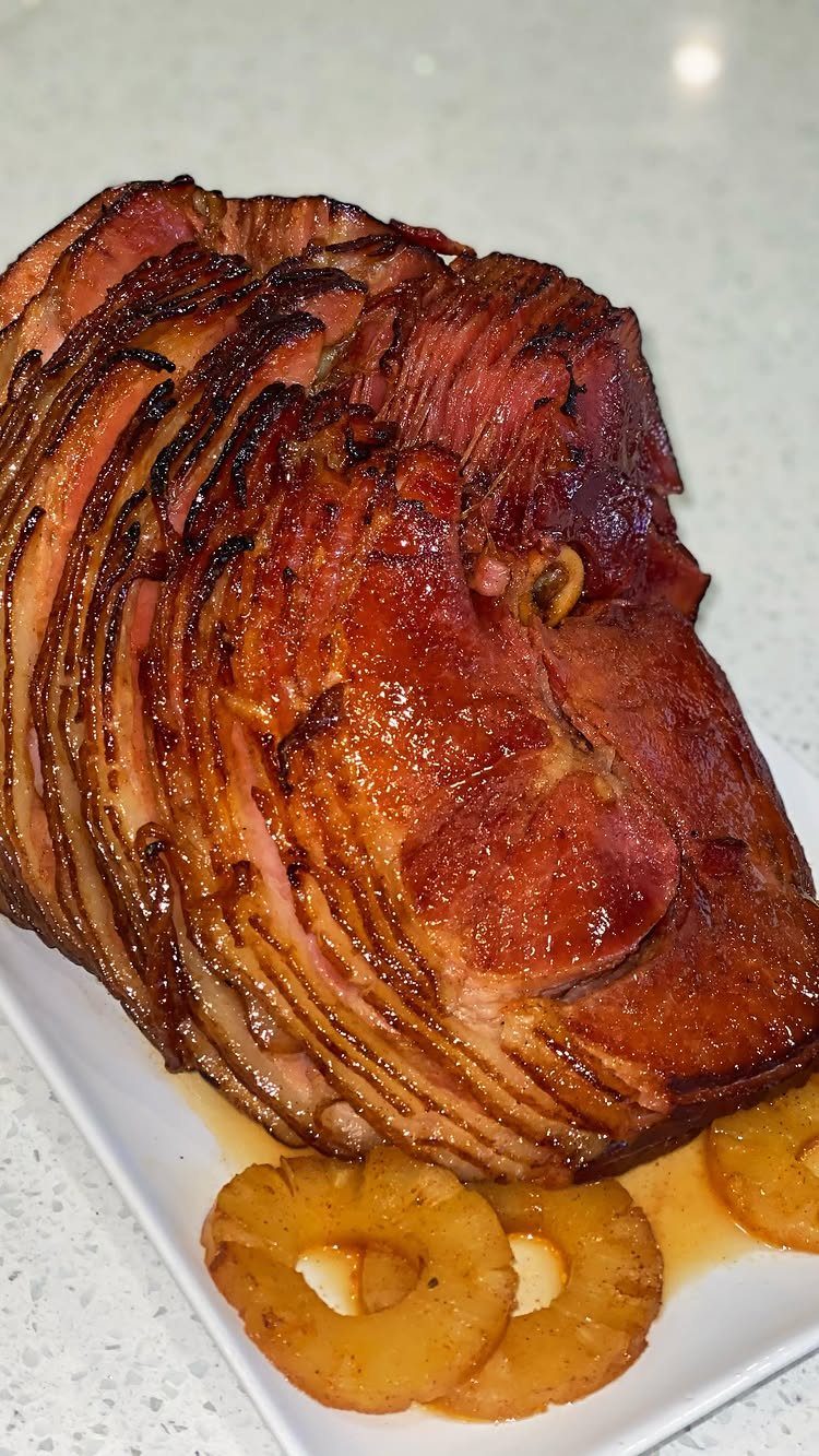 Spiral-sliced glazed ham with pineapple rings on a white rectangular serving platter.