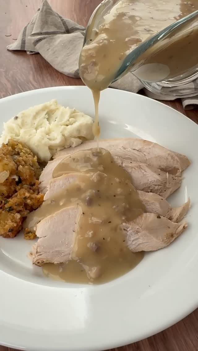 Brown gravy pouring over sliced roast turkey with mashed potatoes and stuffing.