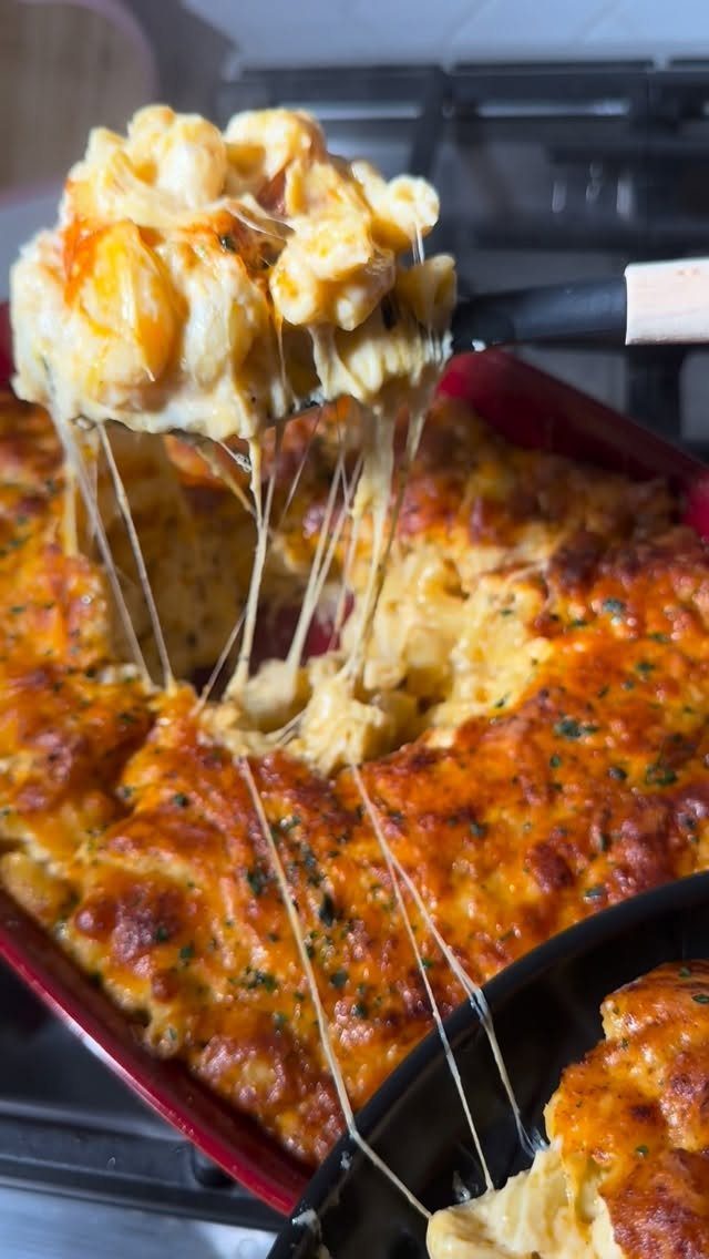 Creamy macaroni and cheese with melted cheese stretching from a red baking dish.