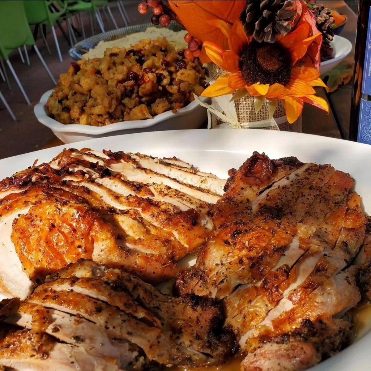 Sliced roast turkey breast on a white platter with stuffing and autumn flowers.