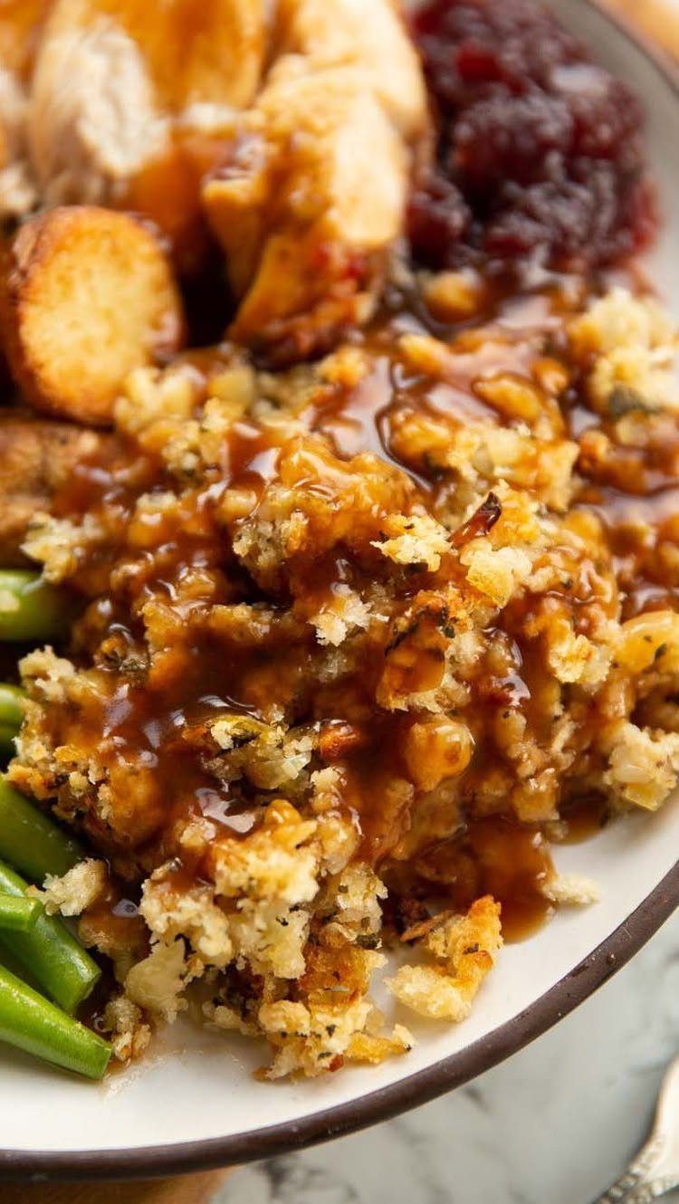 Bread stuffing topped with brown gravy on a plate with turkey and cranberries.