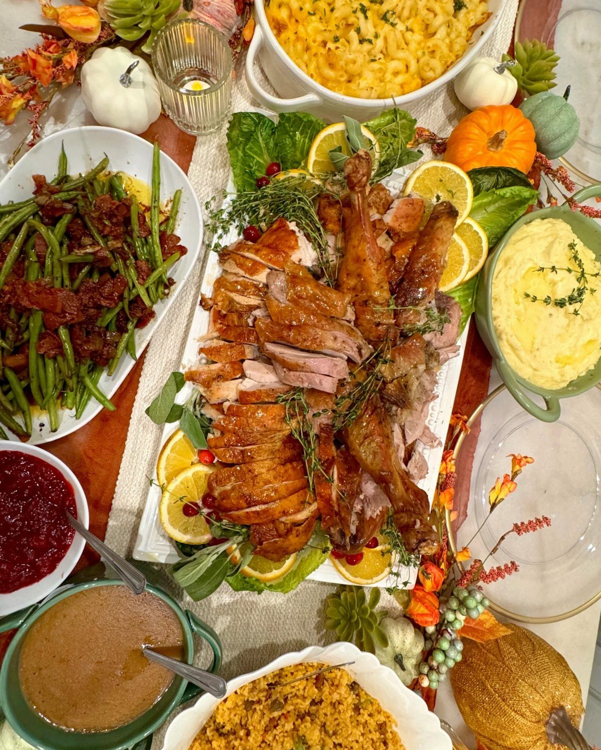 Roasted turkey platter surrounded by traditional Thanksgiving side dishes and autumn pumpkins.