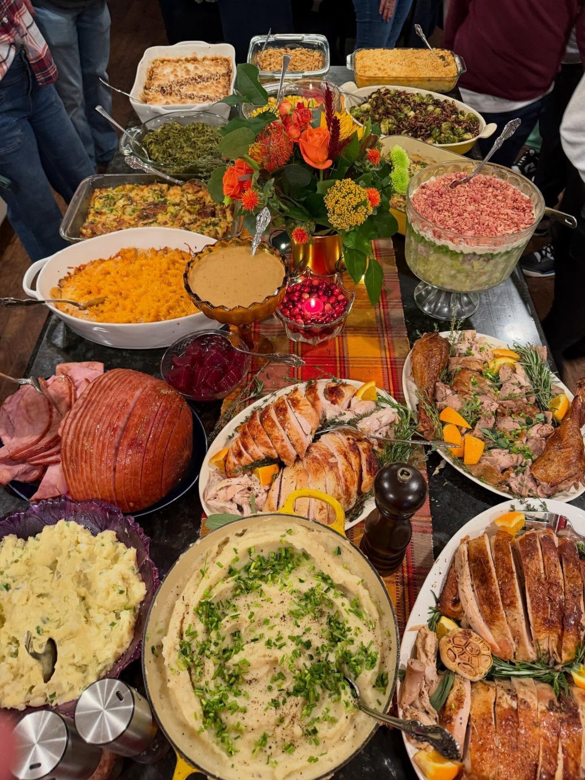 Thanksgiving dinner table spread with roasted turkey, ham, and various seasonal side dishes.