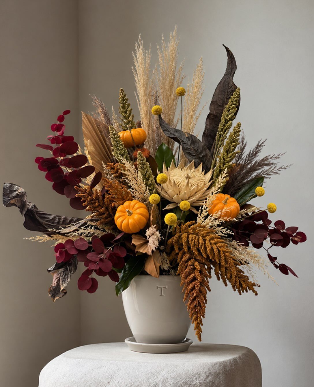 Dried floral arrangement with pampas grass and mini pumpkins in a white vase.