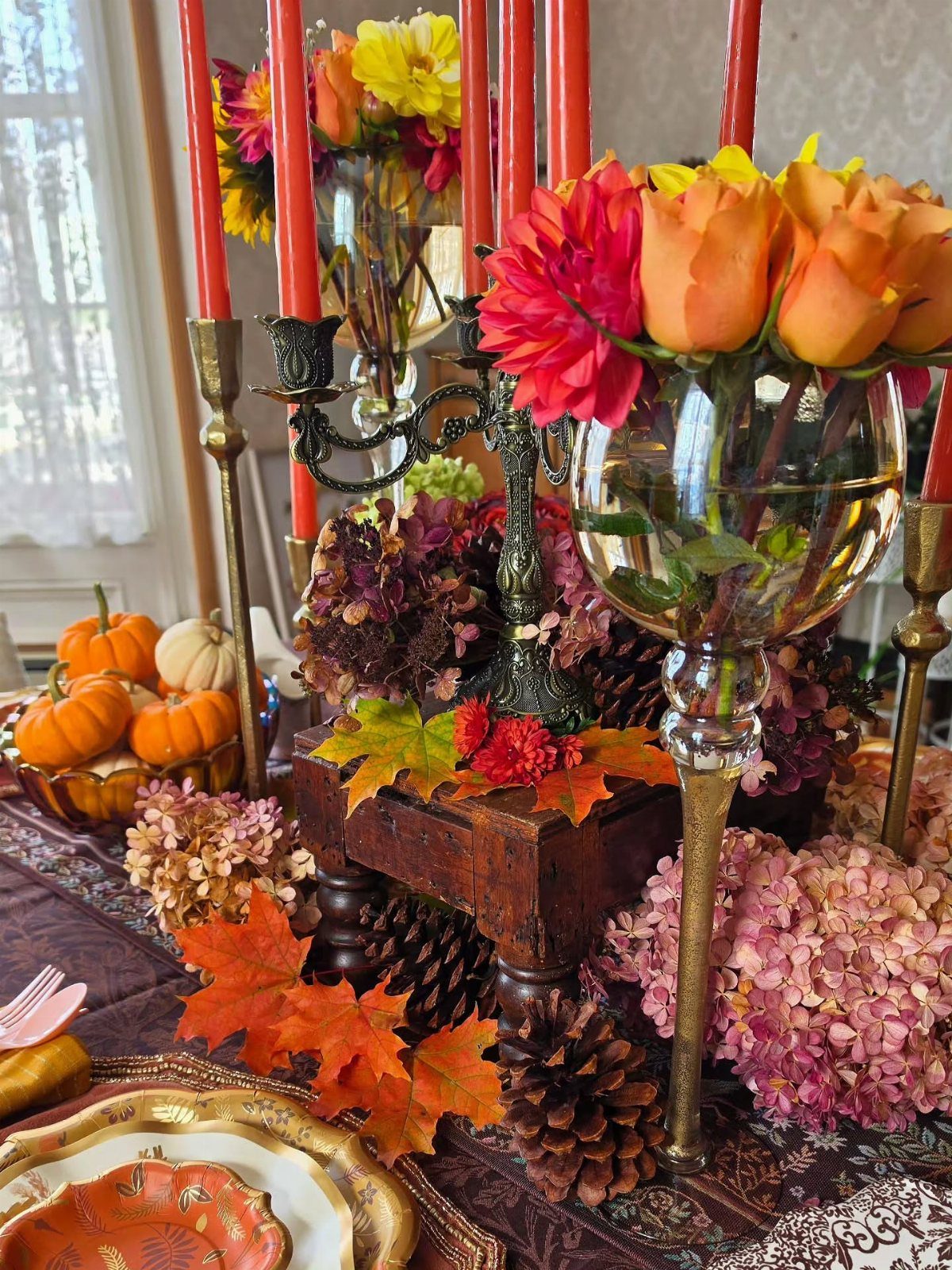 Autumn table setting with orange candles, colorful flowers, and small pumpkins.