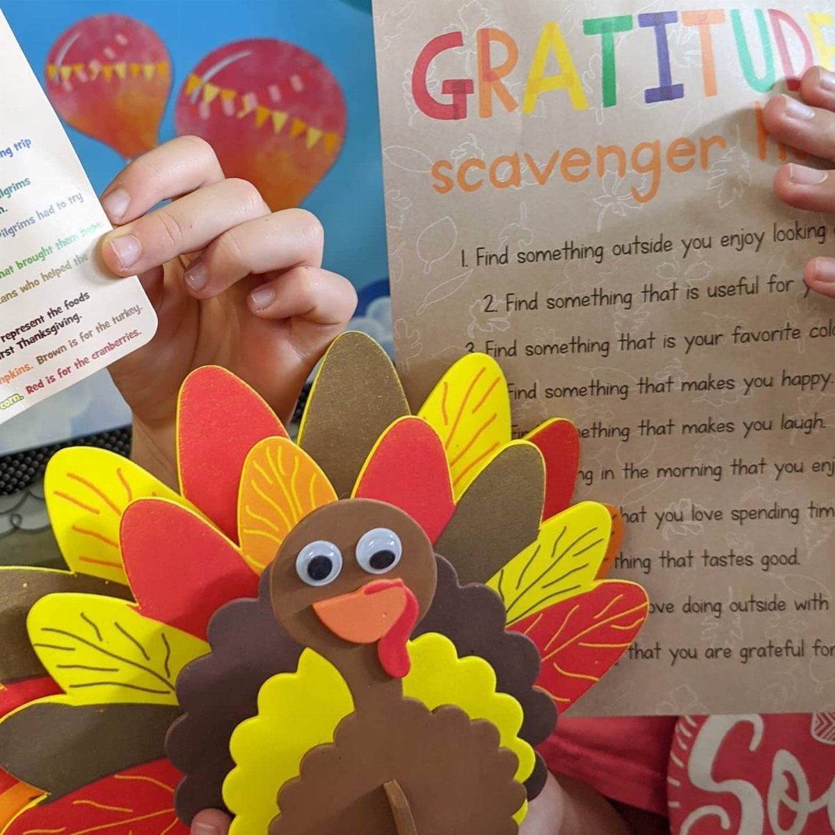 Gratitude scavenger hunt list and a colorful paper turkey craft held by hands.