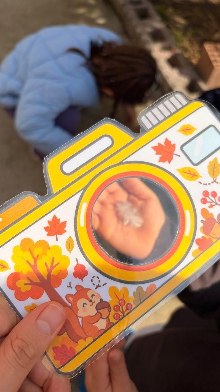 Yellow camera cutout framing a hand holding a small object outdoors.