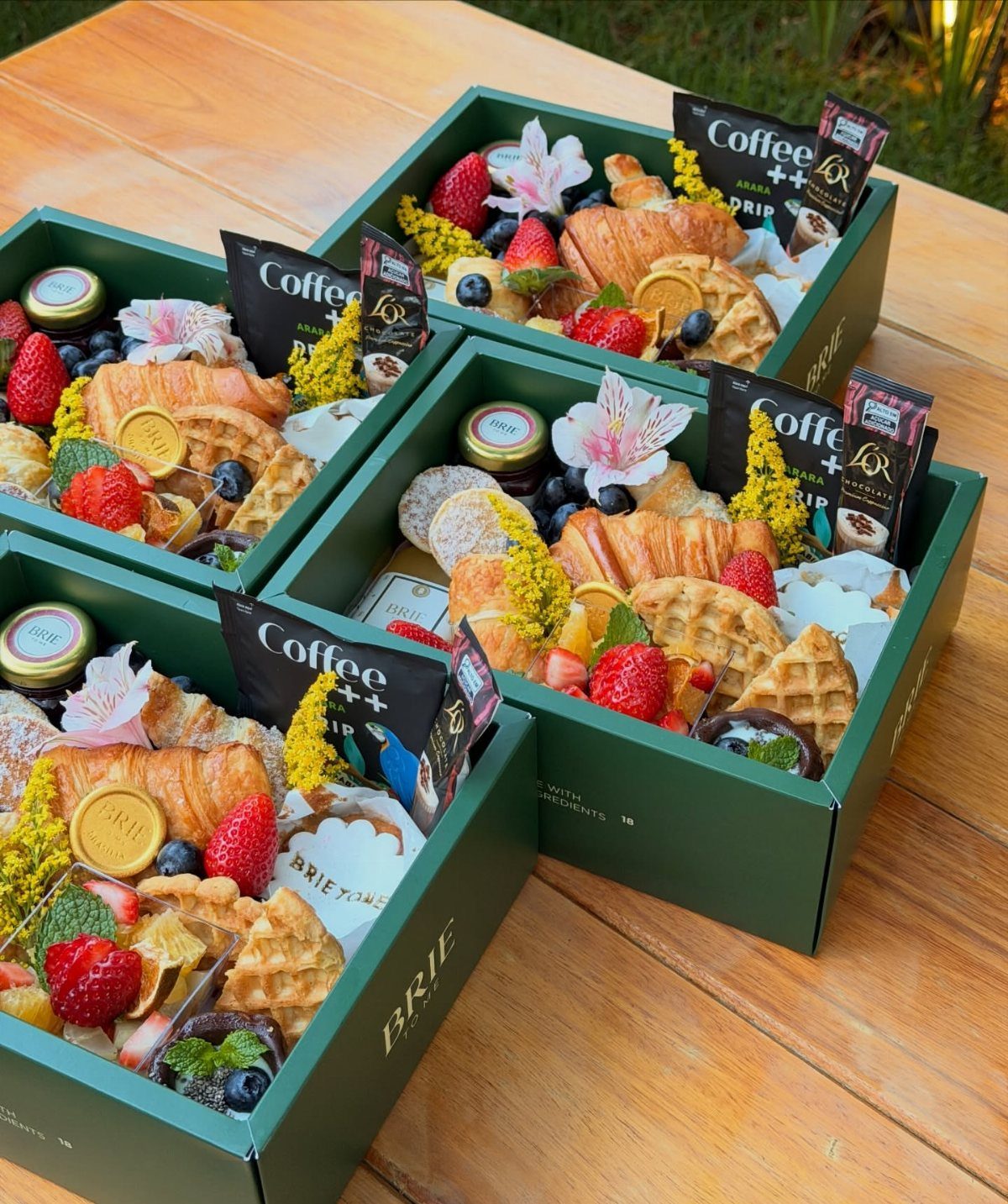Breakfast gift boxes with croissants, waffles, fresh berries, and coffee on wooden table