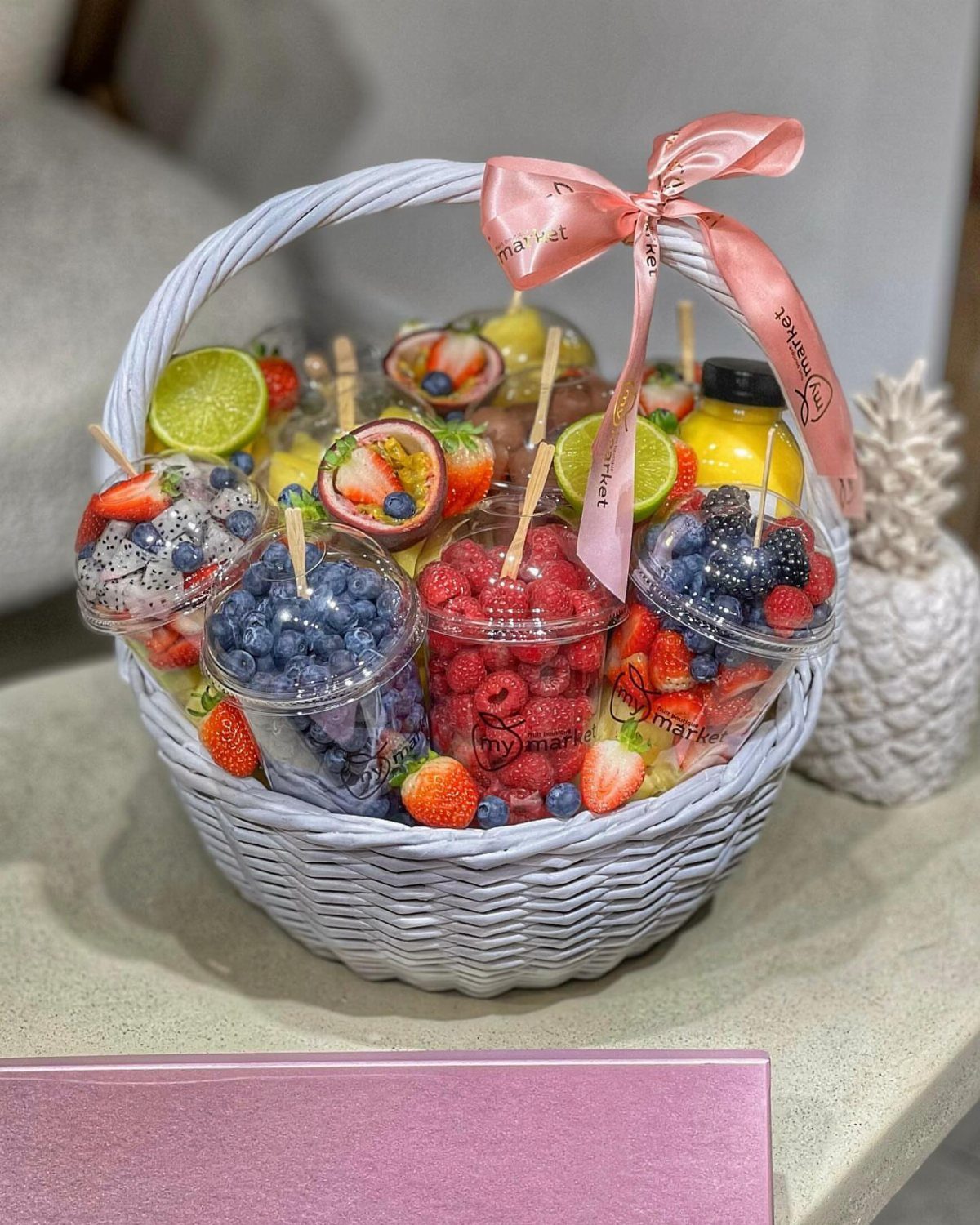 White woven basket filled with cups of fresh berries and lime slices.