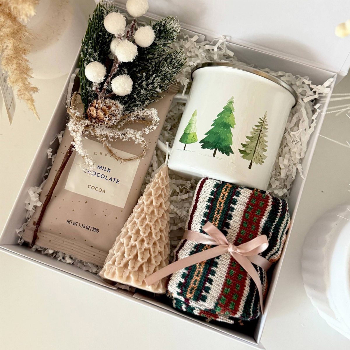 Winter themed gift box with chocolate cocoa, pine tree mug, and knitted accessories.