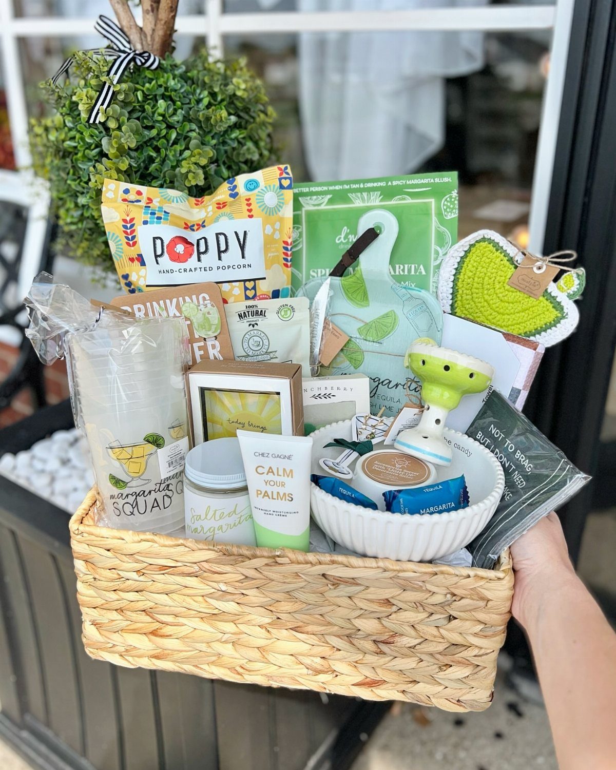 Woven gift basket containing margarita mix, a themed tumbler, and various snacks.