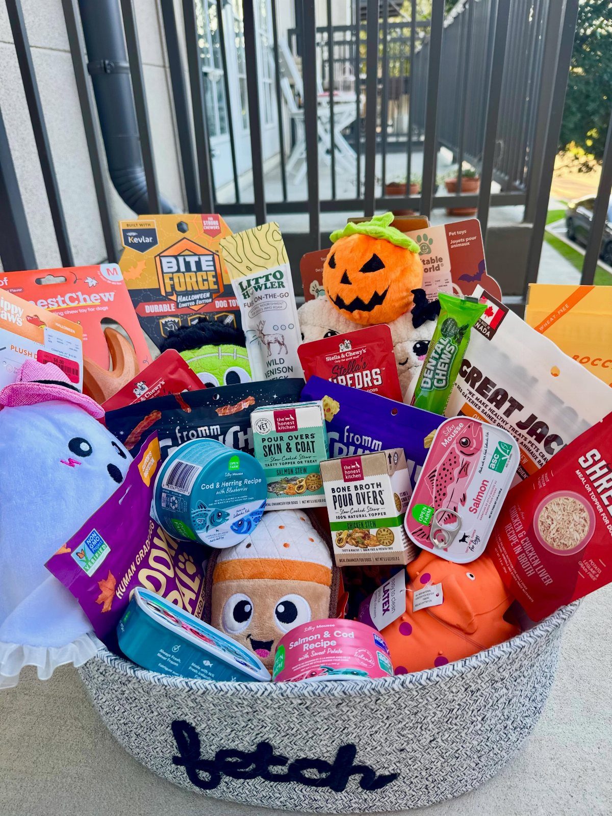 Grey fabric basket filled with dog treats and plush toys for pet owners.
