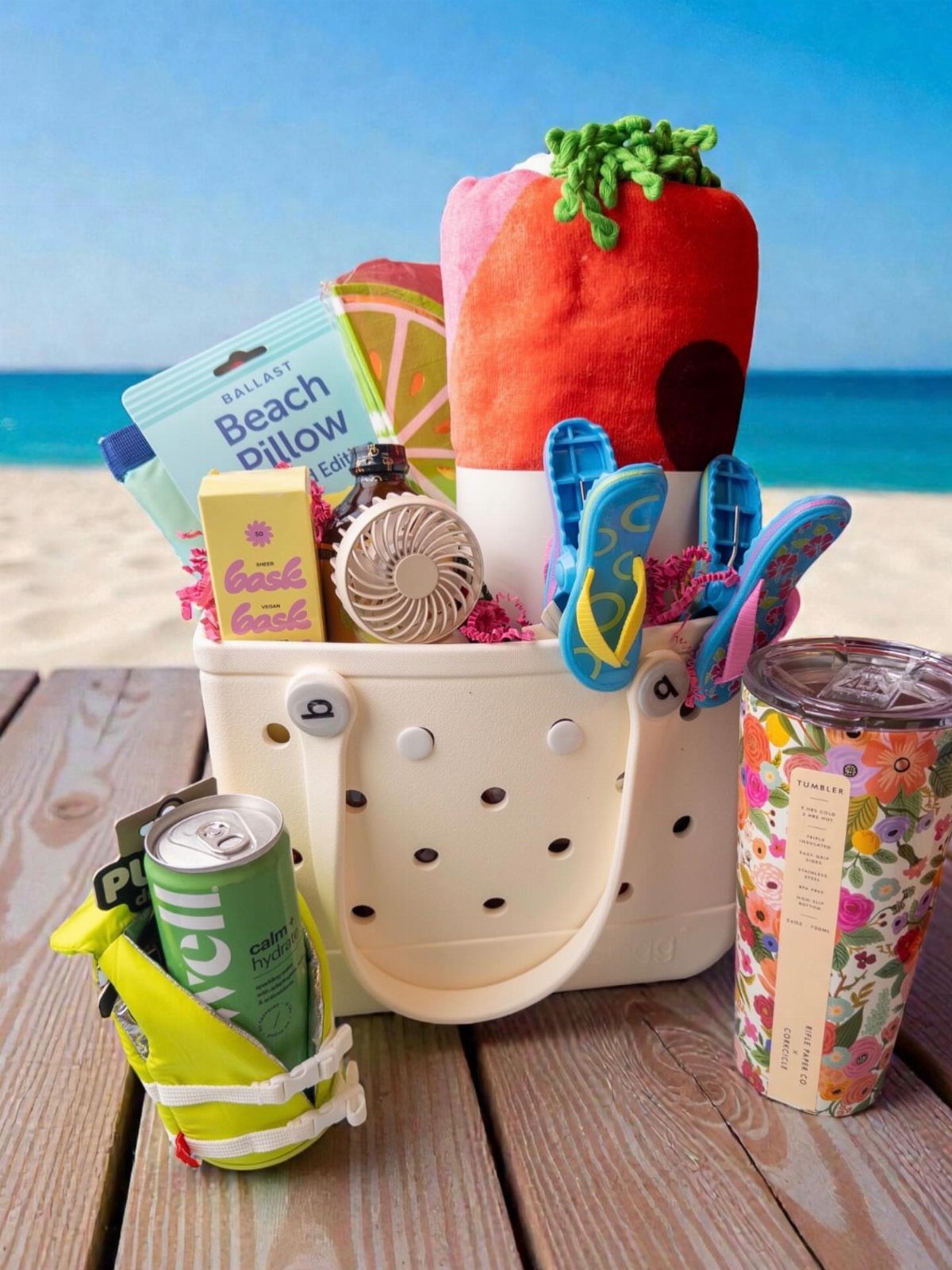 White tote bag filled with beach gear and snacks on a wooden deck.