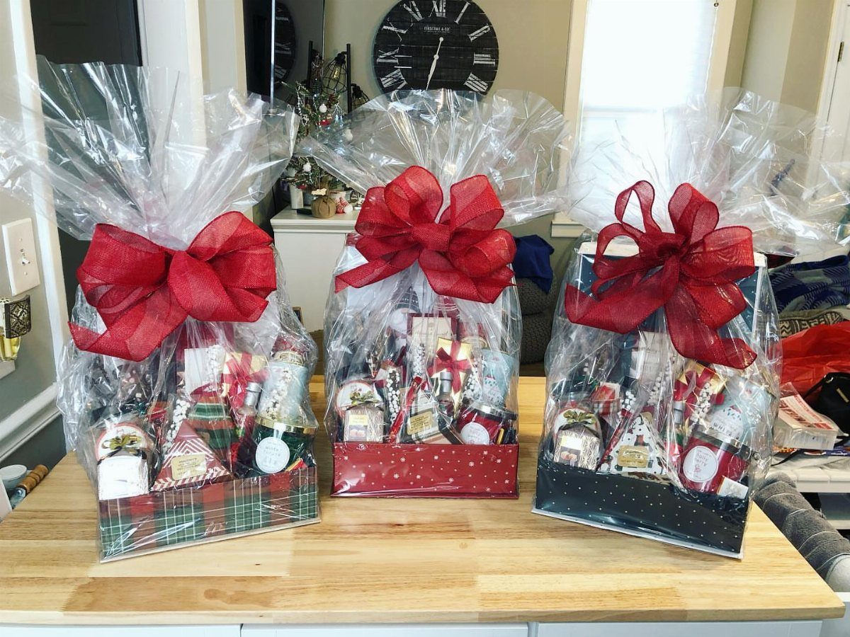 Three cellophane-wrapped gift baskets with red bows containing assorted packaged treats on wood.