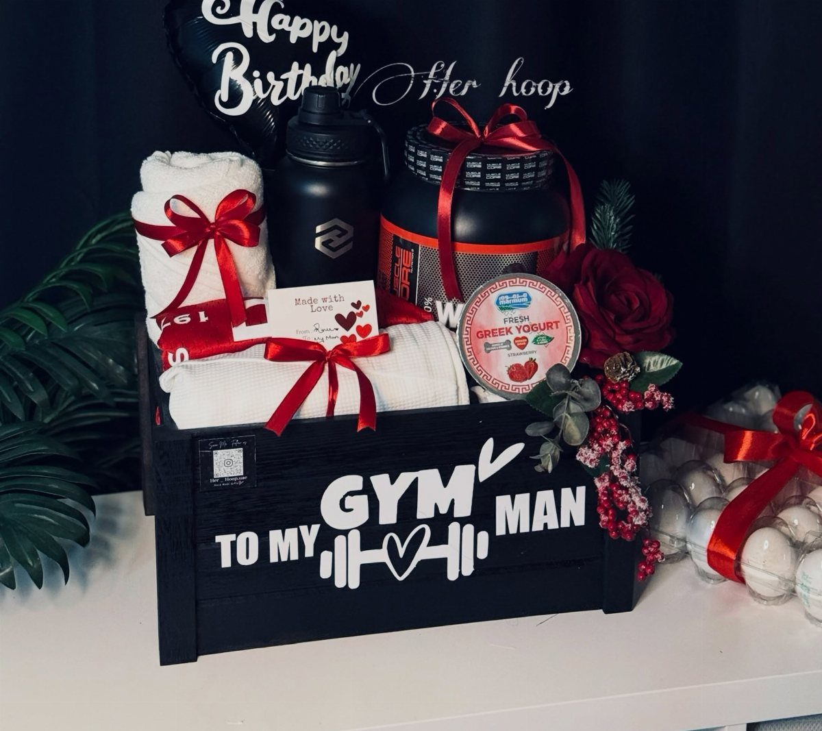 Workout gift basket in a black crate with towels, water bottle, and supplements.
